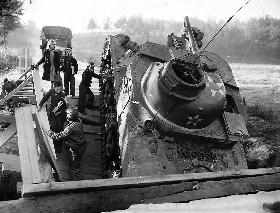 2nd_Armored_Division_Troops_Help_Children_Past_Crashed_M3_lee.jpg